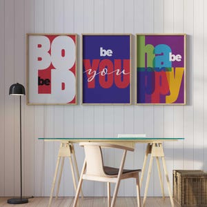 Puede incluir: Tres impresiones artísticas enmarcadas con mensajes inspiradores. La primera impresión dice "BOLD" en letras blancas sobre fondo rojo, con "be" en blanco. La segunda impresión dice "be YOU" en rojo y blanco sobre fondo azul. La tercera dice "be HAPPY" en letras coloridas.