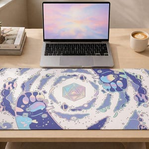 May include: A white desk mat with a colourful, whimsical design featuring blue, purple, and pink elements. The design includes a central geometric shape, stylized clouds, and planets. A laptop, books, and a coffee cup are on the desk.