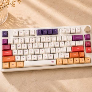 May include: A mechanical keyboard with a white frame and a multi-colored keycap set featuring white, purple, red, and orange keys. The layout includes a circular knob in the top right corner and various icons on the function and modifier keys.