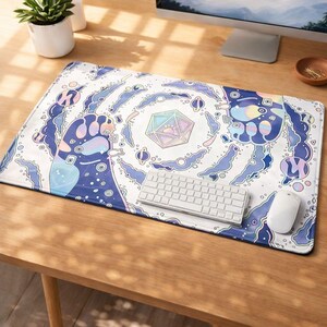 May include: A rectangular white mouse mat with a colourful, whimsical design featuring a large paw print, geometric shapes, and swirling blue and purple elements. A white keyboard and mouse are on the mat.