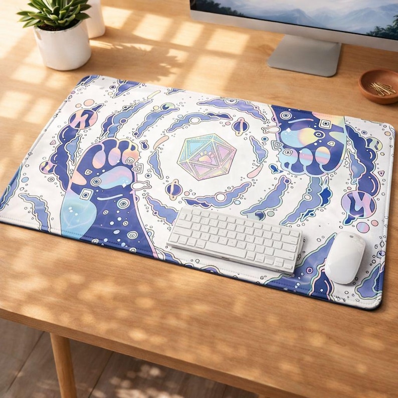 May include: A rectangular white mouse mat with a colourful, whimsical design featuring a large paw print, geometric shapes, and swirling blue and purple elements. A white keyboard and mouse are on the mat.