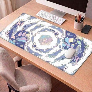 May include: A rectangular white mouse mat with a colourful, whimsical design. The design features a central geometric shape, paw prints, and swirling cloud-like patterns in shades of blue, purple, and pastel colours. A white mouse and keyboard are on the wooden desk.