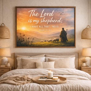 Puede incluir: Una obra de arte enmarcada con el texto "The Lord is my shepherd; I HAVE ALL THAT I NEED. PSALMS 23:1 NLT" contra un paisaje de puesta de sol. La imagen muestra un pastor y ovejas. La obra de arte está sobre una cama.