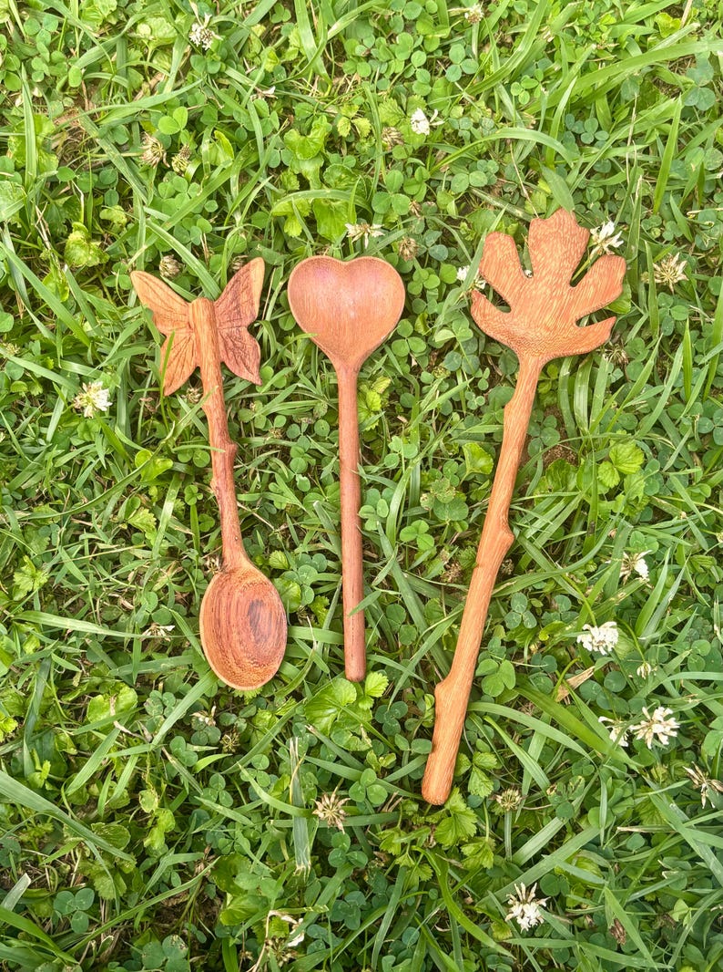 K&ouml;nnte beinhalten: Drei handgeschnitzte Holzl&ouml;ffel mit unterschiedlichen Griffen. Ein L&ouml;ffel hat ein Schmetterlingsmotiv, der zweite eine herzf&ouml;rmige Laffe und der dritte ist mit einem gro&szlig;en Ahornblatt verziert. Jeder L&ouml;ffel hat einen strukturierten, astartigen Griff.