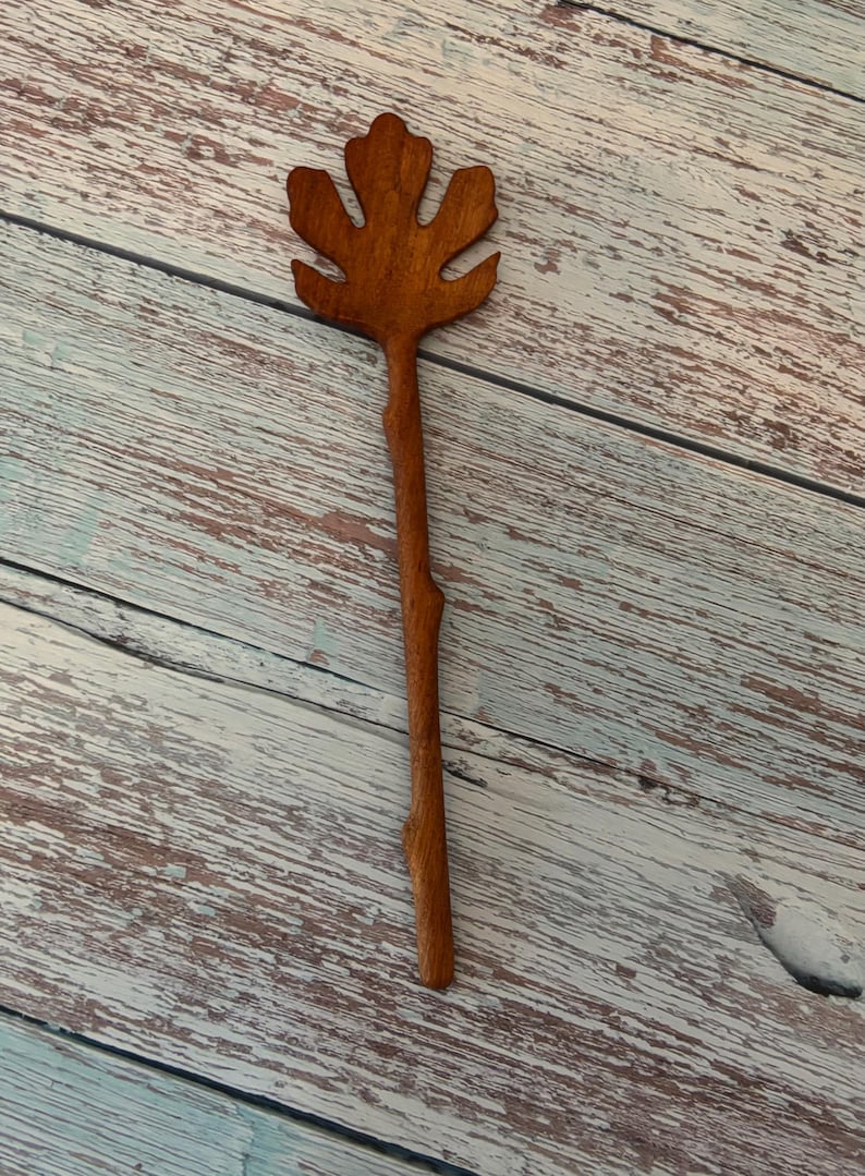K&ouml;nnte beinhalten: Ein brauner Haarschmuck aus Holz mit einem geschnitzten Oberteil in Form eines f&uuml;nfzackigen Feigenblatts. Der Stiel des Haaraccessoires hat eine nat&uuml;rliche, leicht unebene Textur, die an einen kleinen Zweig erinnert, und eine glatte Oberfl&auml;che.