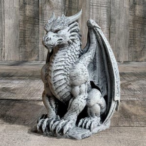 May include: A detailed, gray dragon statue with textured scales, horns, and large wings. The mythical creature is seated, with its claws visible. The statue has a weathered appearance, suggesting an outdoor garden ornament or decorative piece.