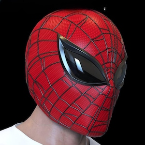 Puede incluir: Una máscara de Spider-Man roja y negra con un diseño de telaraña y grandes cubiertas oculares negras. La máscara está hecha de un material texturizado. La persona que lleva la máscara lleva una camiseta blanca.