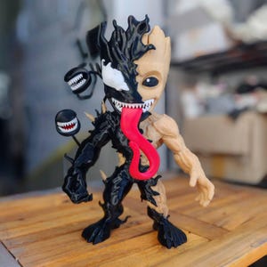 May include: A unique figurine combining the characters Groot and Venom. The figure is split down the middle, with Groot's wooden texture on one side and Venom's black, spiky design on the other. A long red tongue extends from the Venom side.