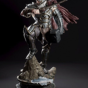 May include: A detailed figurine of a warrior in silver and bronze armor, wielding a sword and hammer. The figure stands atop a rocky base with a red cape, showcasing intricate design and a dynamic pose. The statue is approximately 12 inches tall.