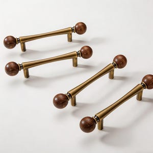 Op de afbeelding: Vier kastgrepen met een messing afwerking en donkere houten kogeluiteinden. De grepen hebben een recht staafontwerp met een lichte curve en zijn geplaatst tegen een witte achtergrond. De houten ballen hebben een rijke, donkerbruine kleur.