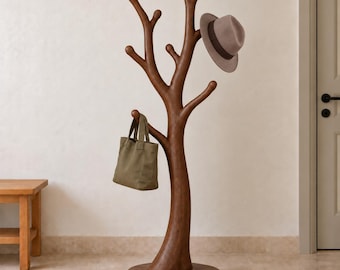 Puede incluir: Un perchero marrón con forma de árbol con múltiples ramas para colgar objetos. Un sombrero fedora gris con una banda oscura está posado en una rama superior, y un bolso de lona verde oliva cuelga de una rama inferior izquierda.
