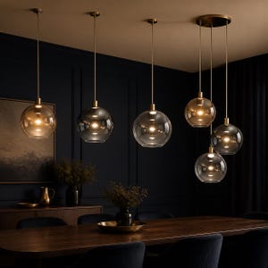 May include: A collection of six pendant lights featuring spherical glass shades in varying amber and clear tones, suspended by thin brass-colored rods from the ceiling. Each globe contains a single illuminated bulb, creating a warm glow.