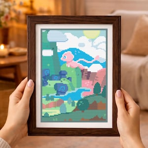 May include: A framed cross-stitch embroidery featuring a pixelated landscape with a pink creature flying above green hills, a blue river, and dark blue trees under a pale yellow sun and white clouds, all enclosed in a dark brown wooden frame.