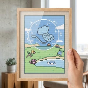 Puede incluir: Un bordado en punto de cruz enmarcado que muestra una criatura pixelada de color azul claro flotando dentro de una burbuja transparente sobre un paisaje verde con un pequeño estanque y varias criaturas pixeladas coloridas sobre el césped.