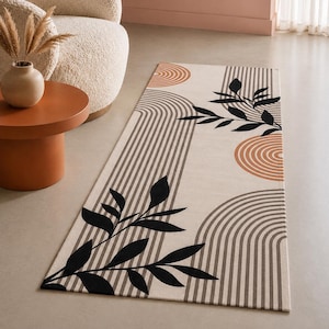 Puede incluir: Una alfombra rectangular con fondo color crema que presenta un patrón de líneas paralelas gris oscuro formando arcos, siluetas de hojas negras y diseños de anillos concéntricos de color terracota sobre toda la superficie.