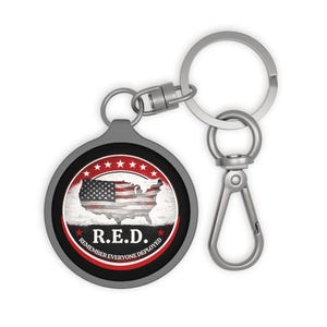 May include: A round metal keychain featuring a graphic of the United States map with a flag pattern. The design includes a red circular border with white stars and the text R.E.D. REMEMBER EVERYONE DEPLOYED in white lettering on a black background.