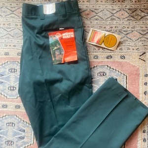 May include: Teal work trousers with a straight leg, featuring a tag that reads "WORK MATE". The trousers are folded neatly, with a second tag visible. The fabric appears to be a durable, wrinkle-resistant material.