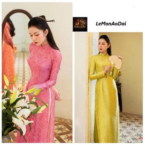 May include: Two women wearing traditional Vietnamese Ao Dai dresses. One dress is a vibrant pink with a floral pattern, and the other is a golden yellow. The dresses have long sleeves and a high collar. The text "LeMonAoDai" is visible.