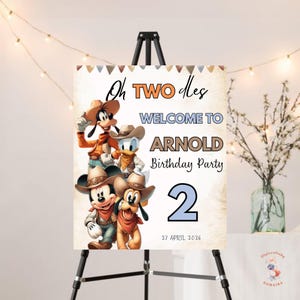 May include: A welcome sign for a birthday party, featuring Disney characters dressed as cowboys. The sign reads "Oh TWO des WELCOME TO ARNOLD Birthday Party 2 27 APRIL 2026". The sign is displayed on a black easel.