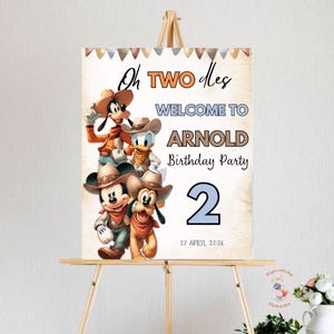 May include: A birthday party welcome sign featuring Mickey Mouse, Goofy, Donald Duck, and Pluto in cowboy attire. The sign reads "Oh TWO les WELCOME TO ARNOLD Birthday Party 2 27 APRIL 2026". The sign is displayed on a wooden easel.