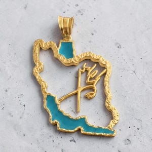 May include: A gold-colored pendant in the shape of a country, with turquoise blue enamel accents. The pendant has a textured border and features gold script. The pendant is likely a piece of jewelry.