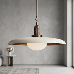 Könnte beinhalten: Eine Pendelleuchte mit einem breiten, flachen, cremeweißen Metallschirm und einer metallischen Innenseite. Das zentrale Element ist eine mattierte Glaskugel, die an einer bronzefarbenen Metallstange mit Haken und zylindrischem Gehäuse hängt.