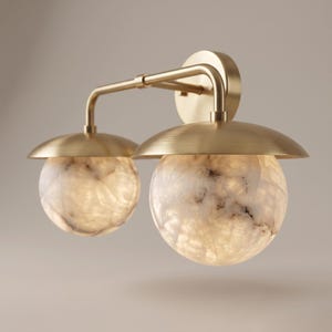 May include: A wall-mounted light fixture featuring a brushed brass finish frame with two horizontal arms extending from a circular base. Each arm supports a dome-shaped brass shade positioned above a spherical, translucent white stone globe light.