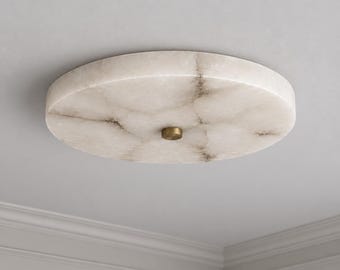 May include: A circular flush mount ceiling light fixture featuring a translucent white alabaster stone shade with natural grey veining patterns. The center of the disc is secured by a small, circular, brushed brass metal hardware component.