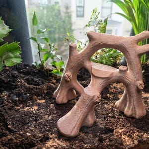 May include: A terracotta-coloured, branch-shaped structure with a textured surface, featuring multiple interconnected limbs and a small, flat platform in the centre, designed as a decorative element for a terrarium or small animal enclosure.