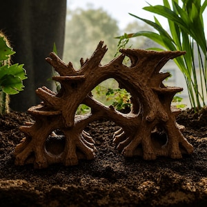 May include: A brown, textured resin structure resembling a gnarled tree root system with multiple arched openings and tiered platforms, designed as a decorative habitat accessory for an enclosure, resting on a dark, loose soil surface.