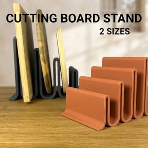 May include: A dark gray and a terracotta-colored cutting board stand, each featuring a wavy, multi-slot design. The text CUTTING BOARD STAND 2 SIZES is visible at the top. The stands are constructed with four vertical slots to hold boards.