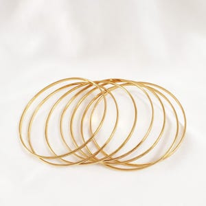 May include: A collection of thin, gold-colored bangles. The bangles are circular and appear to be made of metal. They are arranged in a slightly overlapping pattern against a white background, creating a simple yet elegant aesthetic.