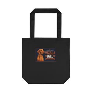 May include: Black tote bag featuring a Vizsla dog illustration and the text "VIZSLA DAD". The design includes the phrase "Happy Father's Day" in a rectangular frame. The bag has two black handles.