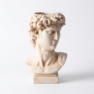 Könnte beinhalten: Eine cremefarbene Keramikbüste einer männlichen Figur mit lockigem Haar, ausgeprägter Kieferpartie und fokussiertem Blick. Die Skulptur verfügt über eine hohle Oberseite, die als Vase dient, und steht auf einem quadratischen Sockel.