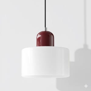Può includere: Lampada a sospensione moderna con paralume cilindrico bianco e parte superiore bordeaux. La lampada è sospesa a un cavo nero e presenta un dettaglio metallico argentato. Design minimalista e contemporaneo.