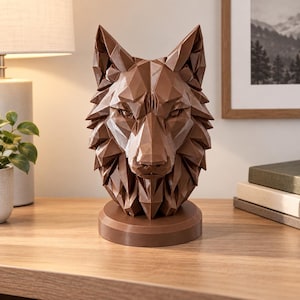 Könnte beinhalten: Eine braune Wolfskopf-Skulptur mit geometrischem, facettiertem Design. Das Objekt ist auf einem runden Sockel montiert und zeigt scharfe, kantige Flächen, die die Ohren, die Schnauze und die Gesichtszüge des Tieres in einer einheitlichen Farbe bilden.