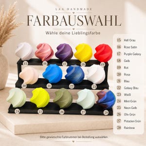 May include: A selection of colorful, swirled decorative objects displayed on a tiered black stand. The image features a color chart with names like "Rose Satin," "Purple Galaxy," and "Rainbow." The text "FARBAUSWAHL" and "LAA HANDMADE" are also visible.