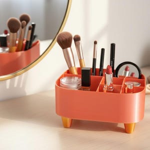 Könnte beinhalten: Ein orangefarbener Make-up-Organizer mit mehreren Fächern, der verschiedene Make-up-Pinsel, Lippenstifte und einen kleinen Spiegel enthält. Der Organizer hat kurze, gelb-orangefarbene Beine. Ein runder Spiegel und eine kleine Topfpflanze befinden sich im Hintergrund.