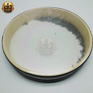以下が含まれることがあります： 白い表面と小さな銀色のビーズの縁取りがある丸い楽器。縁はベージュで、白と黒のストライプの縁があります。「ZamJ Crafts」のロゴが見えます。