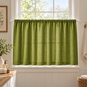 May include: A solid olive green cafe curtain with a textured, woven appearance hangs from a white rod. The fabric features vertical folds and a straight hem, covering the lower portion of a window while allowing light to pass through.