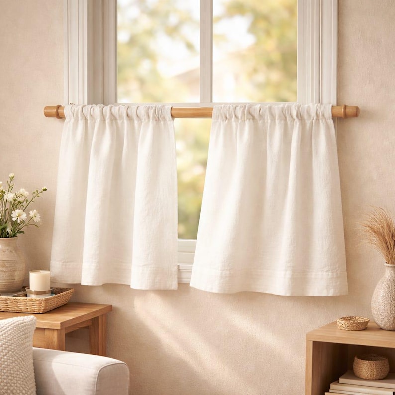 Puede incluir: Un par de cortinas de caf&eacute; de color blanco roto colgadas de una barra de madera clara. Las cortinas presentan una parte superior fruncida y un borde inferior con dobladillo, cubriendo la parte inferior de una ventana.