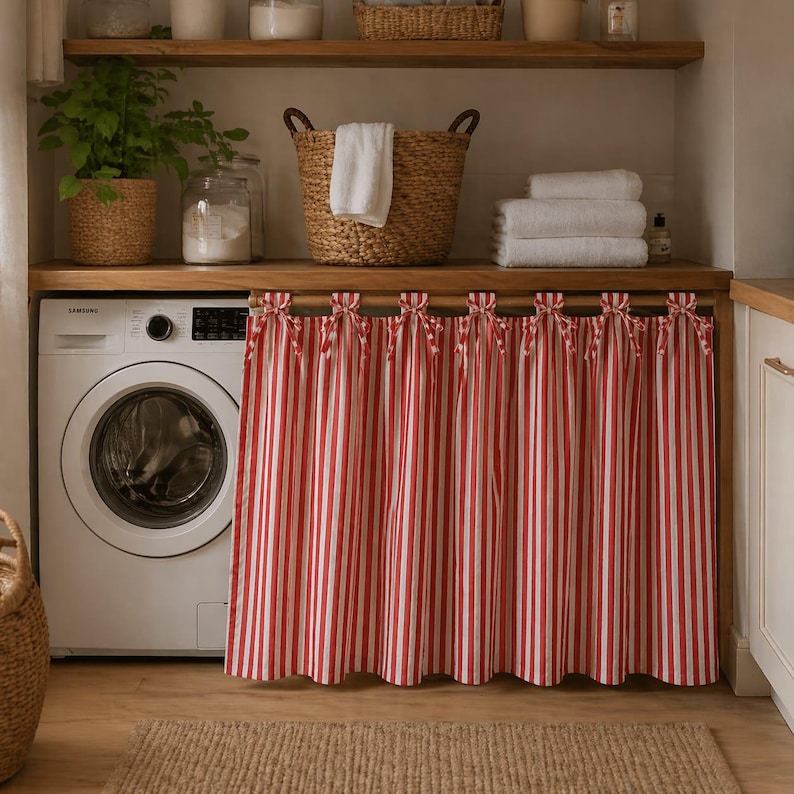 May include: A laundry room scene featuring a white washing machine, wooden shelves, and a red and white striped curtain. A woven basket holds a white towel, and a potted plant adds a touch of greenery. The room has a warm, inviting aesthetic.