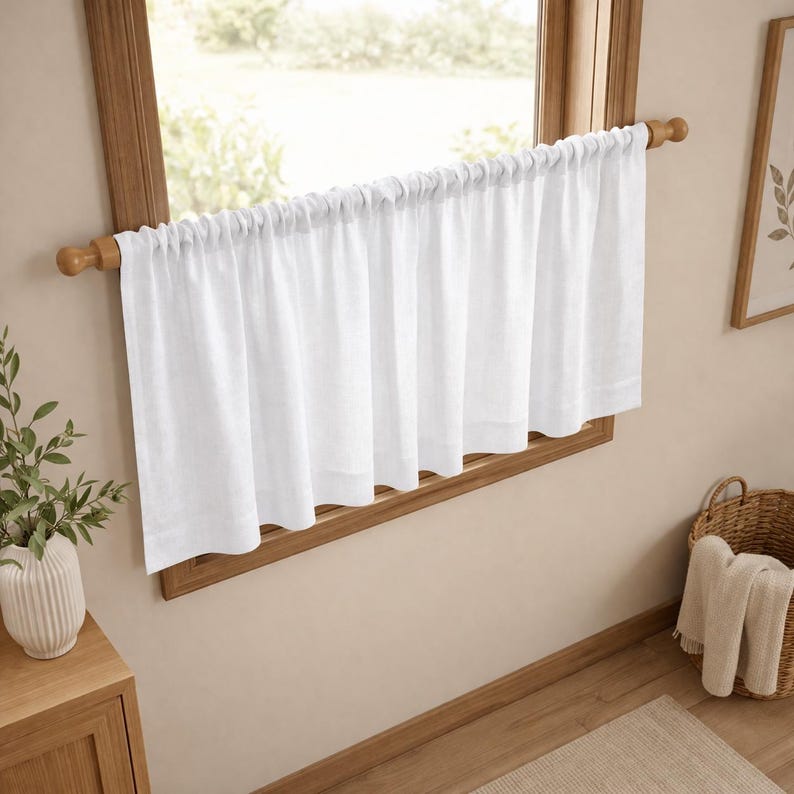 Puede incluir: Una cortina de caf&eacute; blanca y lisa cuelga de una barra de madera montada dentro del marco de la ventana. La cortina presenta un encabezado fruncido y un dobladillo recto, proporcionando una ligera cobertura en la parte inferior.