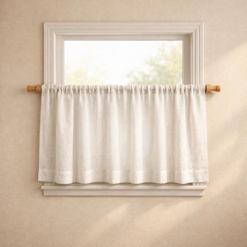 Puede incluir: Una cortina de caf&eacute; de color beige claro cuelga de una barra de madera con remates decorativos. La cortina presenta un dise&ntilde;o fruncido y plisado que cubre la parte inferior del marco de una ventana, aportando una textura suave y neutra.