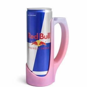 May include: A Red Bull energy drink can held in a pink mug-shaped holder. The can is blue and white with the Red Bull logo. The holder has a handle and is a gradient of pink and white.