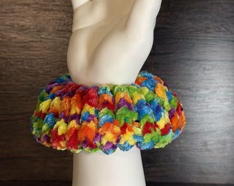 Könnte beinhalten: Ein dickes, flauschiges Haargummi aus weichem, fusseligem Garn mit einem lebendigen, mehrfarbigen Muster in Rot, Orange, Gelb, Grün, Blau und Violett. Das kreisförmige Haaraccessoire hat eine dichte, strukturierte Optik mit gerafftem Design.