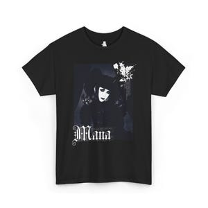 Puede incluir: Camiseta negra con un gráfico en blanco y negro de una persona con maquillaje dramático y un sombrero. La palabra "Mana" está escrita en una fuente decorativa debajo de la imagen. La camiseta está hecha de un material suave.