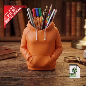 Könnte beinhalten: Ein orangefarbener Schreibtisch-Organizer in Hoodie-Form, gefüllt mit Stiften und Bleistiften. Der Organizer hat eine Vordertasche und weiße Kordelzüge. Ein rotes Banner zeigt "3D STL FILES DIGITAL DOWNLOAD". Ein ledergebundenes Buch und eine Lupe sind ebenfalls sichtbar.