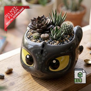 May include: A black ceramic planter shaped like a dragon's head, with yellow eyes, filled with succulents and small stones. The planter has a 3D STL files digital download tag.