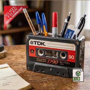Könnte beinhalten: Ein Schreibtisch-Organizer in Form einer Vintage-Kassette vom Typ TDK D90. Der rechteckige Behälter hat ein rot-weiß-schwarzes Etikett mit dem Text TDK, A, 90 und D90. Er enthält verschiedene Stifte, einen Bleistift und einen Radiergummi. Ein rotes Banner zeigt 3D STL FILES DIGITAL DOWNLOAD.